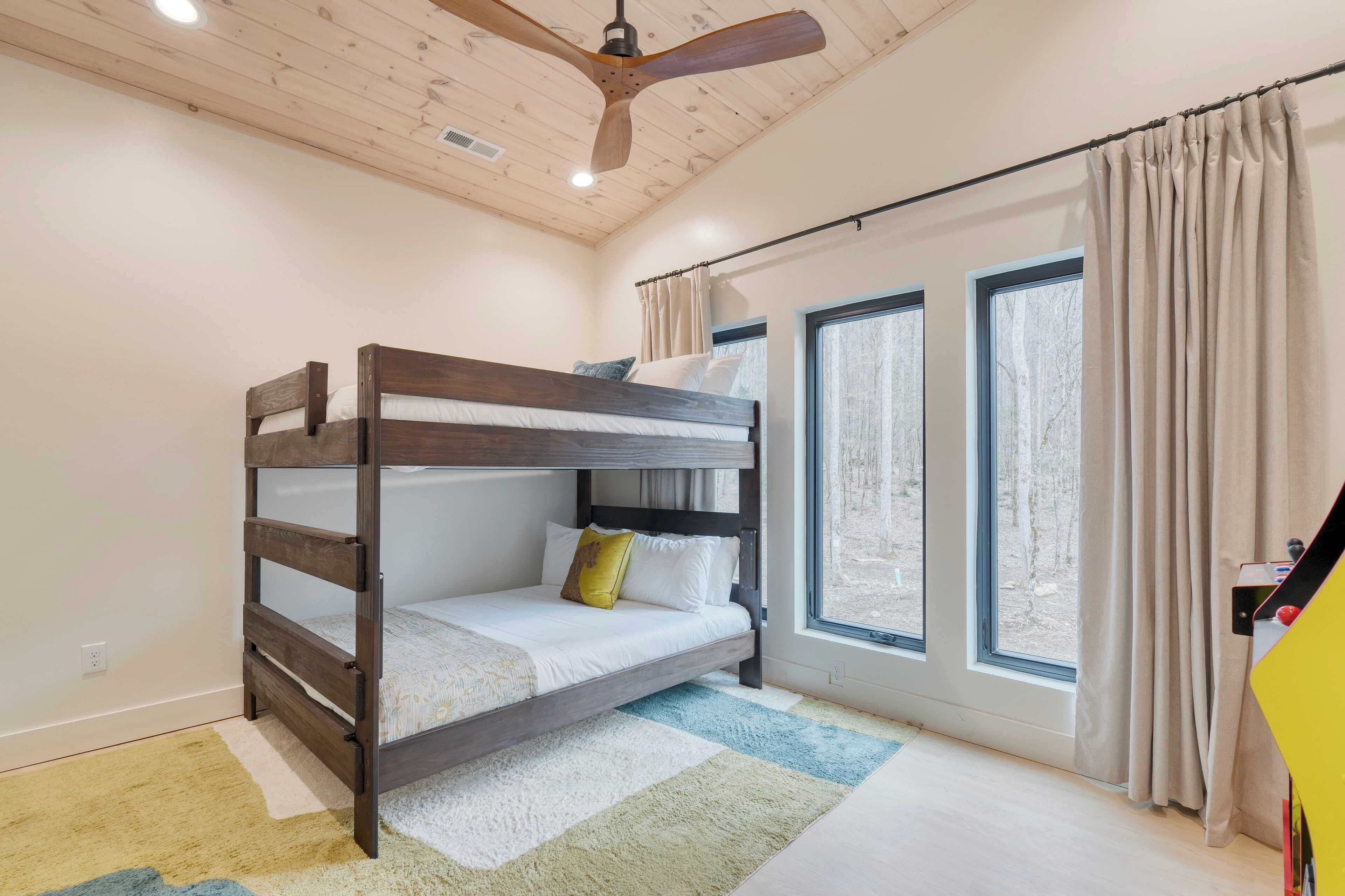 Una cama individual en un dormitorio con ventilador de techo, ventanas amplias y vistas al exterior.