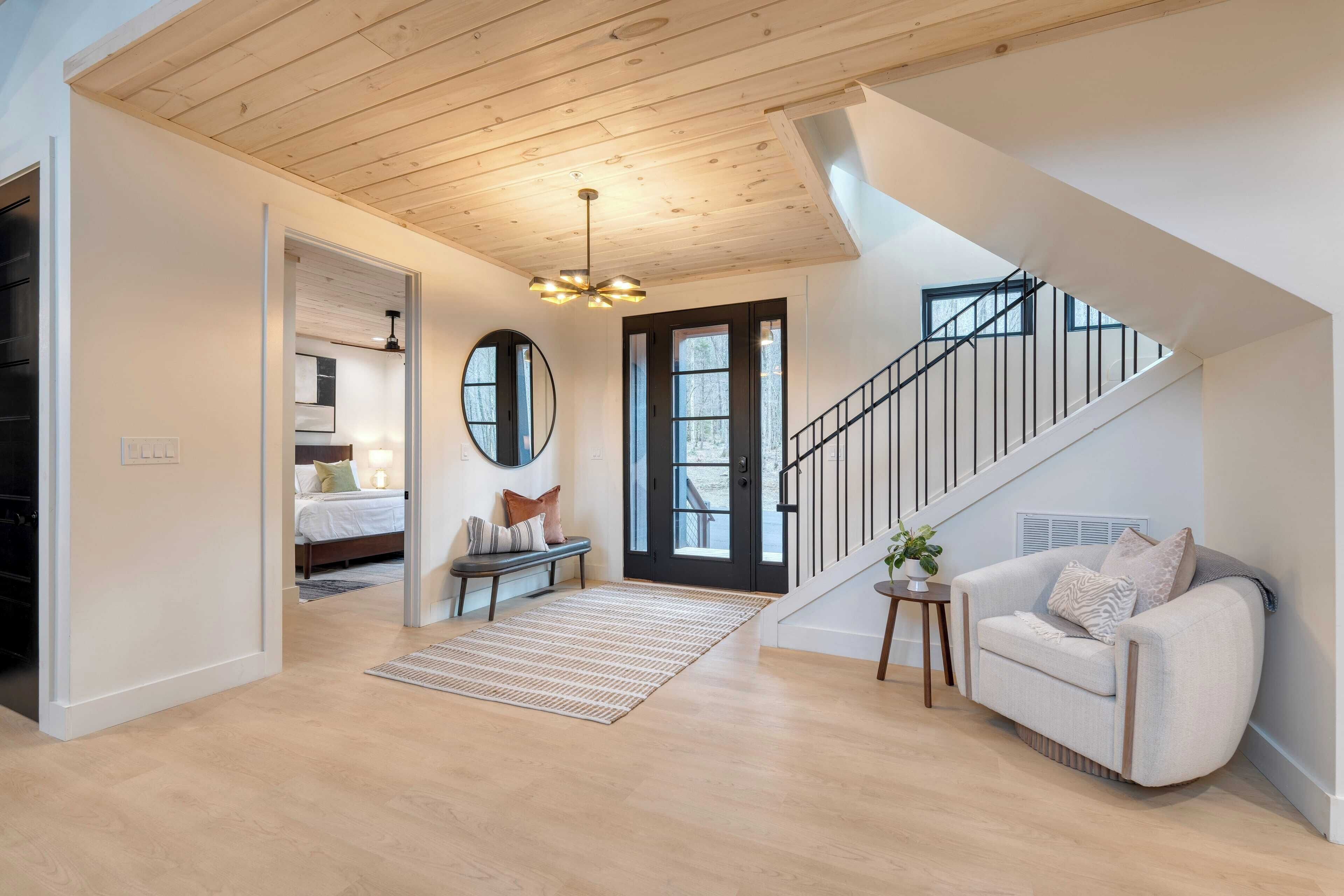 A spacious living area with a wooden ceiling, a staircase, a sofa, and a bench.
