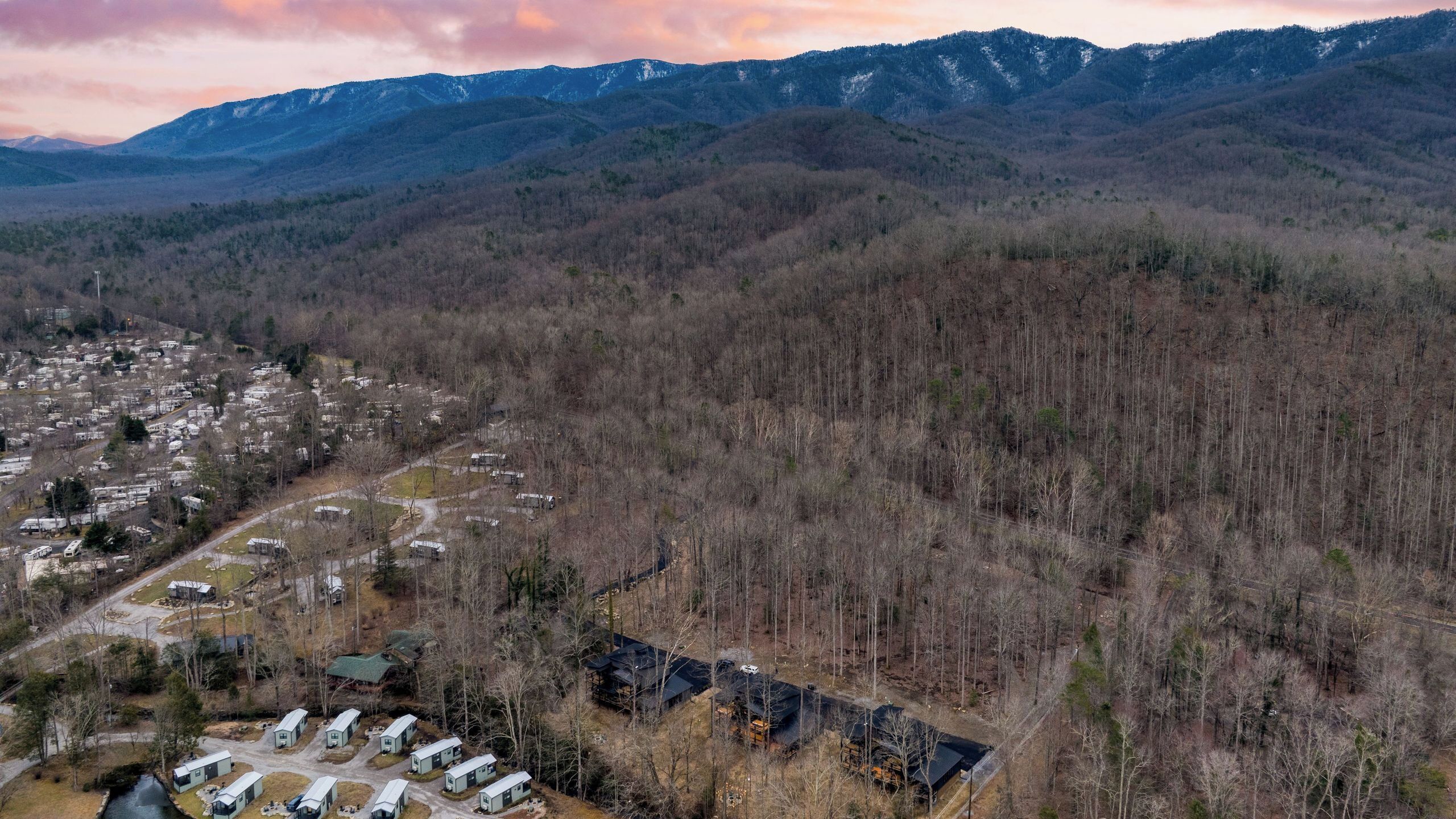 An aerial view of a campground with RVs and cabins, surrounded by forested hills.