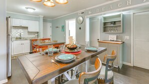 A dining area with a wooden table set for four, surrounded by chairs. A kitchen with white cabinets and a countertop is visible in the background. - Golf, Shop & Relax Beachside! Hilton Head Getaway (Hilton Head Island)