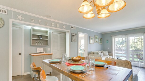 A dining area with a wooden table set for four, surrounded by chairs. A kitchen area is visible to the left with a counter and shelves. - Golf, Shop & Relax Beachside! Hilton Head Getaway (Hilton Head Island)