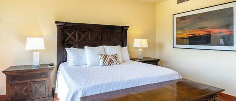 A bedroom with a large bed, two bedside tables, a wooden bench, a patterned rug, and a framed picture on the wall.