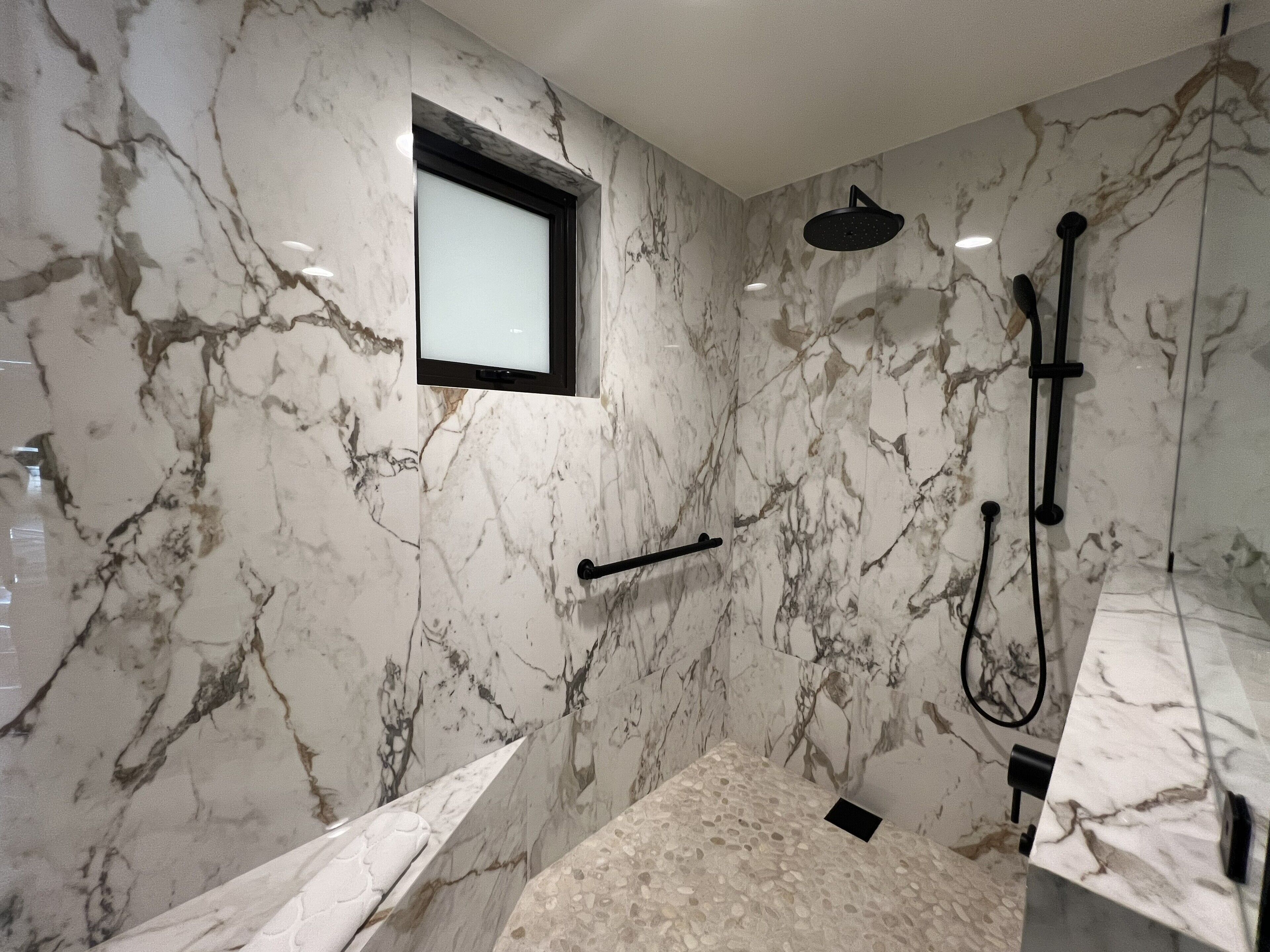 A modern bathroom with marble walls, a built-in window, a shower area, and a bathtub.