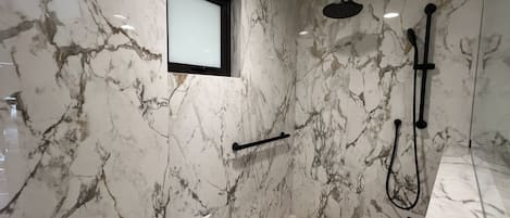 A modern bathroom with marble walls, a built-in window, a shower area, and a bathtub.