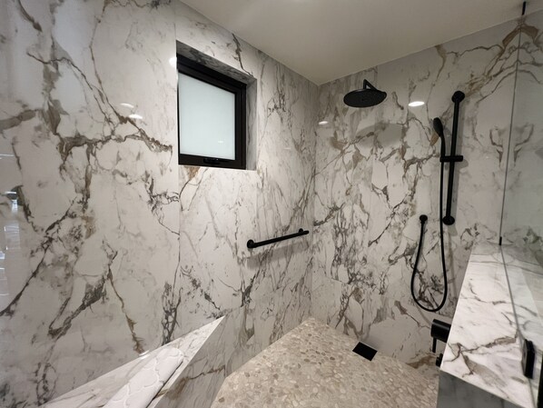 Un baño moderno con paredes de mármol, un ventanal integrado, zona de ducha y bañera.