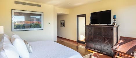 Een slaapkamer met een groot bed, een televisie op een houten dressoir en een ingelijst kunstwerk aan de muur.