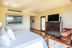 A bedroom with a large bed, a television on a wooden cabinet, and a framed picture on the wall.
