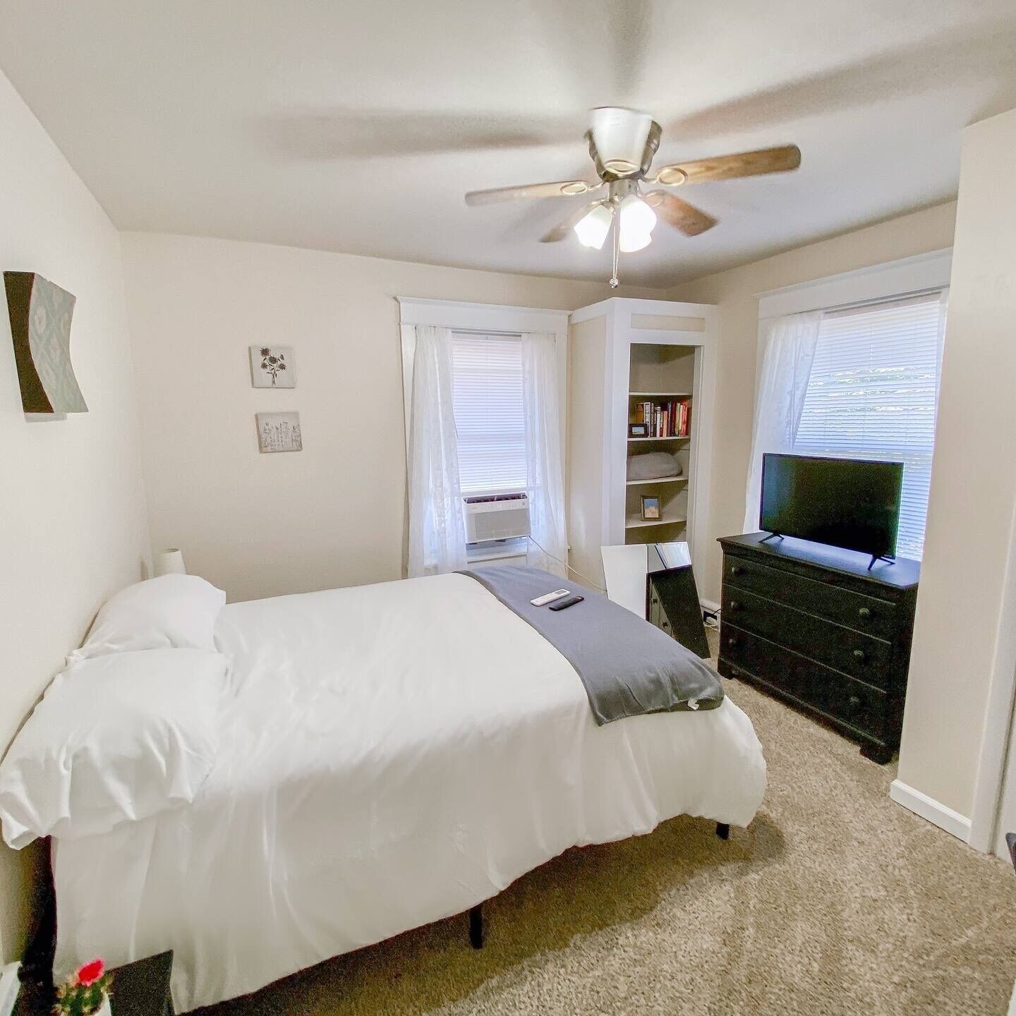 A bedroom with a bed, a ceiling fan, a bookshelf, and a TV.