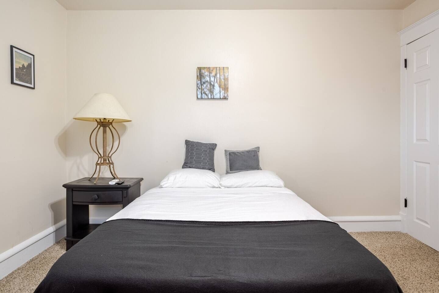 A bedroom with a bed, a nightstand, a lamp, and a picture on the wall.