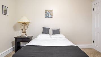 A bedroom with a bed, a nightstand, a lamp, and a picture on the wall.