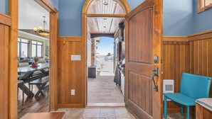 A wooden interior with a dining area, a blue chair, and a view through an open door. - Snow Therapy Chalet Ski In Out & Hot Tub (Big White)
