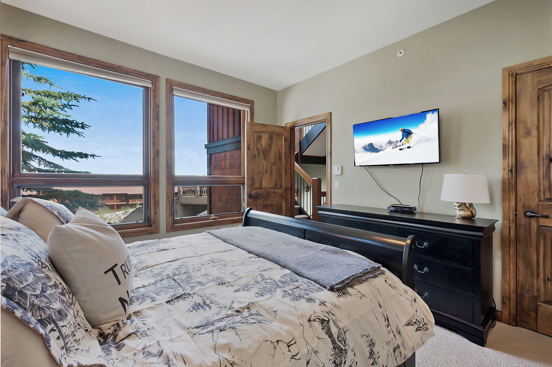 Quarto com cama grande, televisão, cômoda e vista para o exterior.