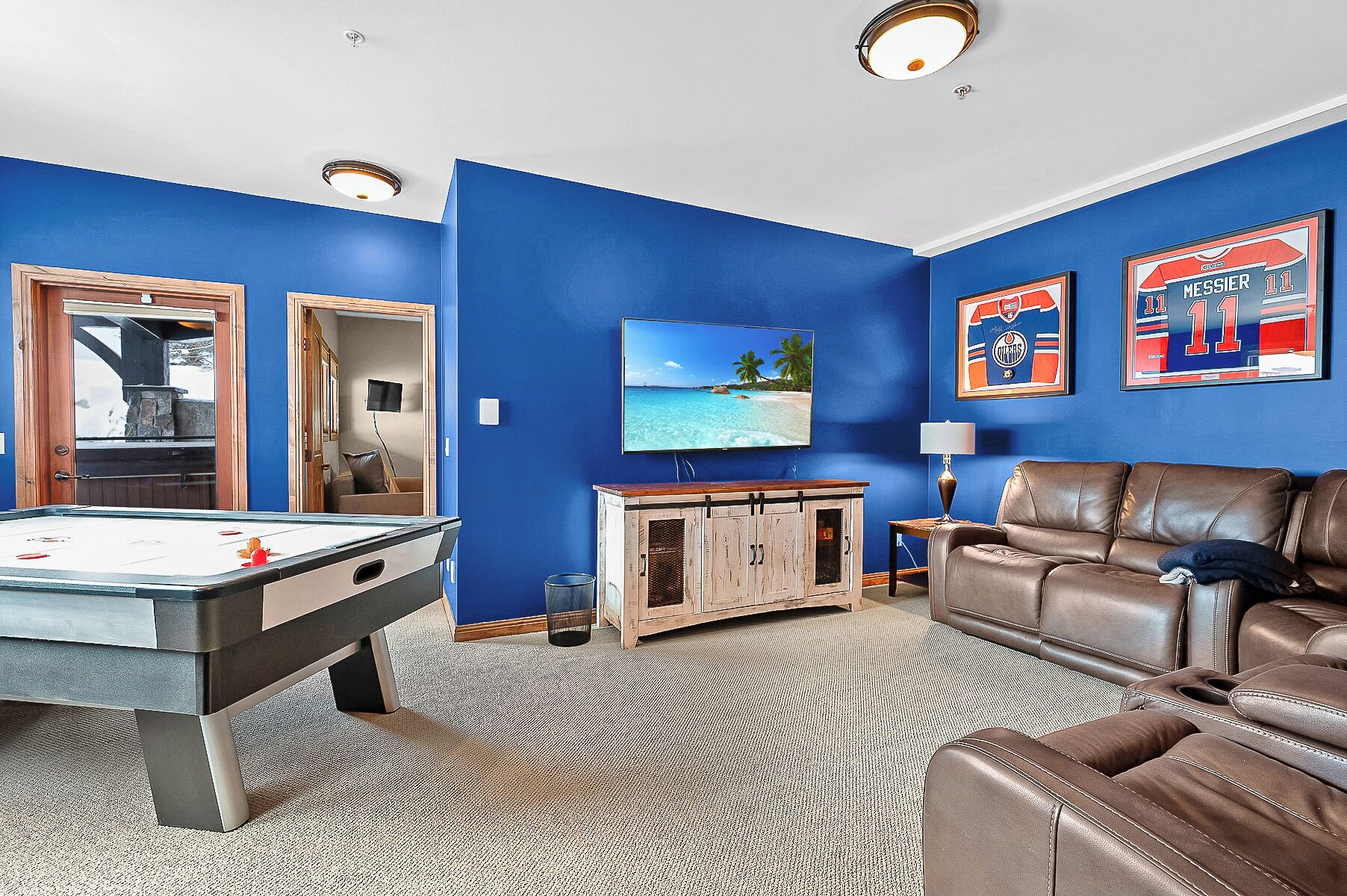 A room with a pool table, a leather couch, and a television on the wall.
