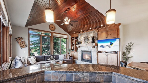 A spacious living area with a stone fireplace, a large TV, and a ceiling fan. - Snow Therapy Chalet Ski In Out & Hot Tub (Big White)