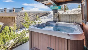 A hot tub under a wooden pergola with a stone wall and a sign indicating a view of mountains. - Snow Therapy Chalet Ski In Out & Hot Tub (Big White)
