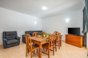 Un espace repas comprenant une table en bois, des chaises, un canapé, un téléviseur et un meuble.