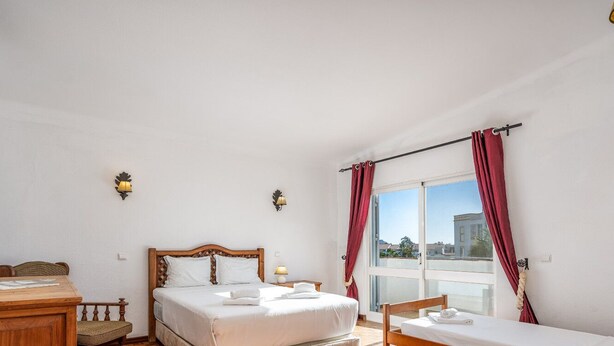 Habitación de hotel con cama, escritorio, silla, ventana con cortinas y vistas a edificios.