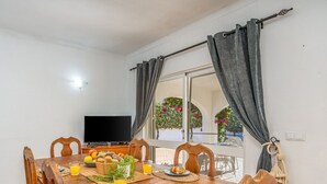 Un comedor con una mesa preparada para el desayuno, un televisor y vistas a un balcón con plantas.