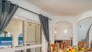 Un área de comedor con una mesa de billar, sillas de madera y una mesa dispuesta con frutas y bebidas.