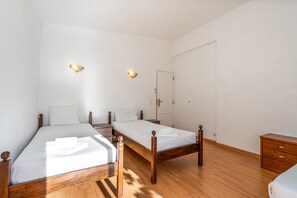 Une chambre avec deux lits simples, une commode en bois et une porte.
