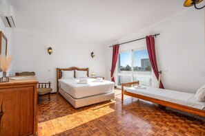 Ein Zimmer mit Bett, Schreibtisch, Stuhl, einem Fenster mit Vorhängen und Blick nach draußen.