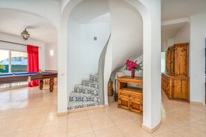 A spacious room with a pool table, a staircase with patterned tiles, and a wooden cabinet.