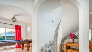 Una habitación con mesa de billar, una escalera con baldosas estampadas y un armario de madera.