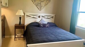 A bedroom with a bed, a nightstand, a lamp, a decorative wall piece, and a window with curtains.