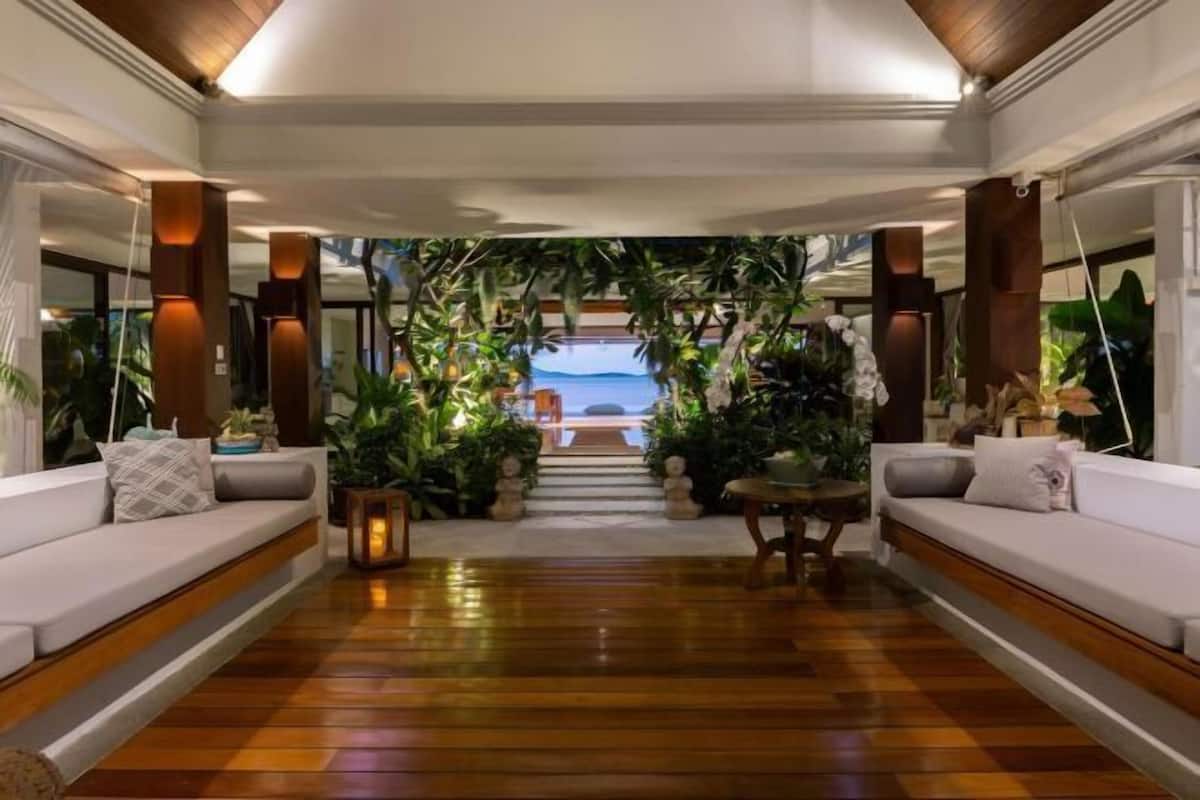 Un pasillo con piso de madera, sofás blancos y vista al océano a través de un ventanal.