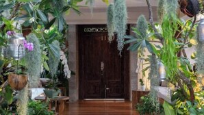 A wooden door with a sign above it, surrounded by lush greenery and hanging plants. - Chic Baan Capo - Luxury Four Bedroom Beachfront Villa (Koh Samui)