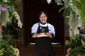A person holding a plate with food, standing in a room with plants and a wooden floor.