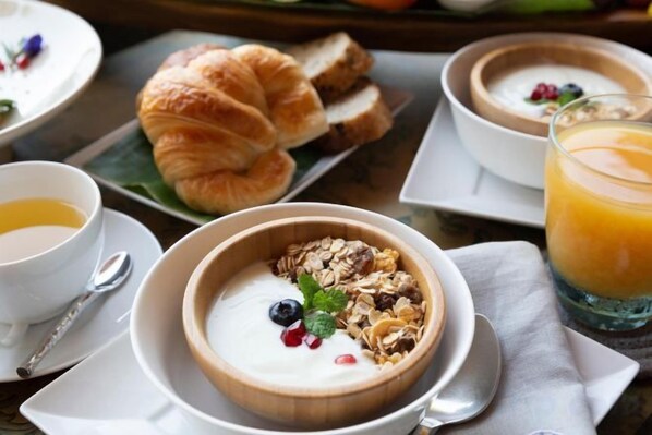 A breakfast setting with bowls of yogurt and granola, a croissant, and a glass of orange juice.