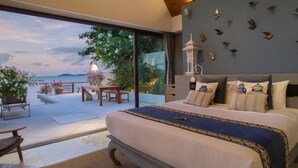 A bedroom with a large bed, a view of the outdoors, a dining area, and a wall with decorative elements. - Chic Baan Capo - Luxury Four Bedroom Beachfront Villa (Koh Samui)
