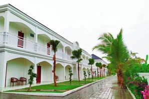 Stunning hotel with a symmetrical facade, featuring arches and balconies with railings, set amidst a beautifully maintained garden with palm trees.