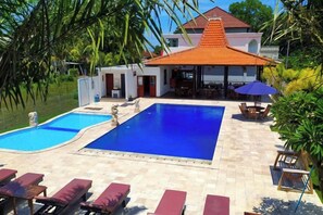 A hotel with a swimming pool, lounge chairs, and a covered outdoor seating area. - Puri Lovina Hotel (Bali)