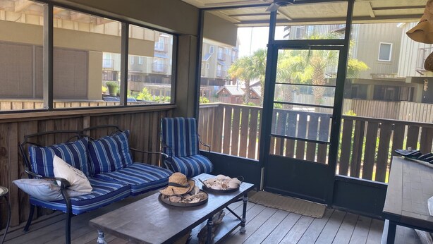 Un patio techado con terraza de madera, un sofá azul a rayas y una mesa con un sombrero y pan.