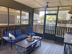Une terrasse couverte avec une plateforme en bois, un canapé à rayures bleues et une table sur laquelle se trouvent un chapeau et du pain.