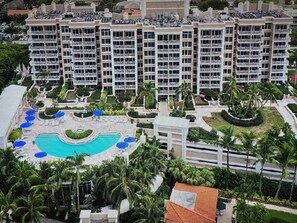 Un hôtel à plusieurs étages doté d’une piscine, de palmiers et d’un jardin bien entretenu.