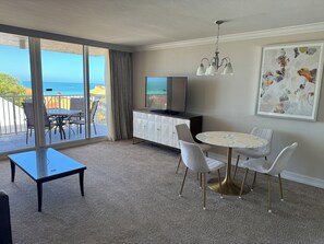 Une chambre d’hôtel avec un balcon, une table à manger avec des chaises, une télévision et un tableau au mur.