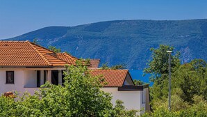 A building with a red-tiled roof and white walls, surrounded by greenery and overlooking a mountainous landscape. - Semi-detached holiday house DIVNA with private pool (Pinezići)