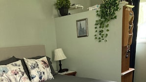 Un letto rifatto con una coperta grigia, due cuscini floreali, una lampada da comodino e un piccolo comodino in legno.