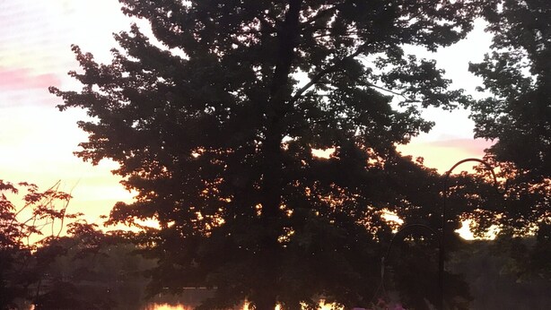 Un pontile di legno con tavolo e sedie, affacciato su uno specchio d'acqua con un tramonto sullo sfondo.