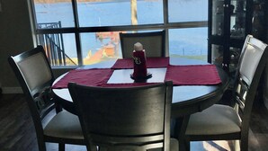 Un'area pranzo con un tavolo apparecchiato per quattro persone, una finestra vista lago e una libreria con oggetti decorativi.
