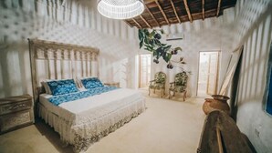 A bedroom with a large bed, two chairs, a hanging plant, and a rustic ceiling. - Angel de Santa Fe by Bernalo Hotels (Santa Fe de Antioquia)