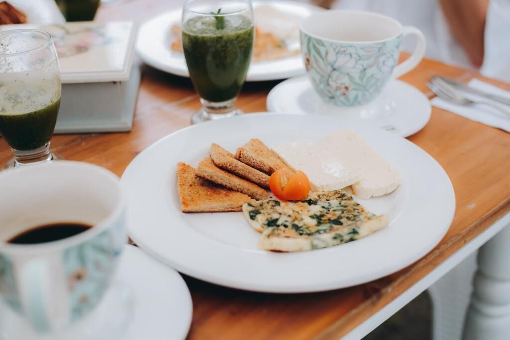 A breakfast setting with toast, a tomato, scrambled eggs, and a green smoothie on a table.