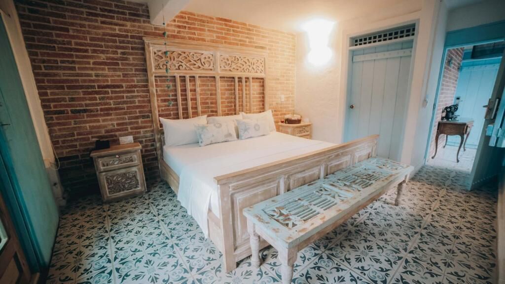 Un dormitorio con pared de ladrillo, cama con cabecero de madera, una banca y suelo estampado.