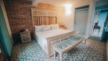 Een slaapkamer met een bakstenen muur, een bed met houten hoofdbord, een bankje en een vloer met een patroon.