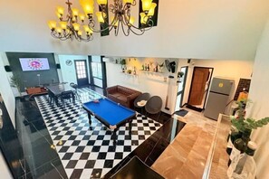 Un salon avec une table de billard, un canapé et un lustre.