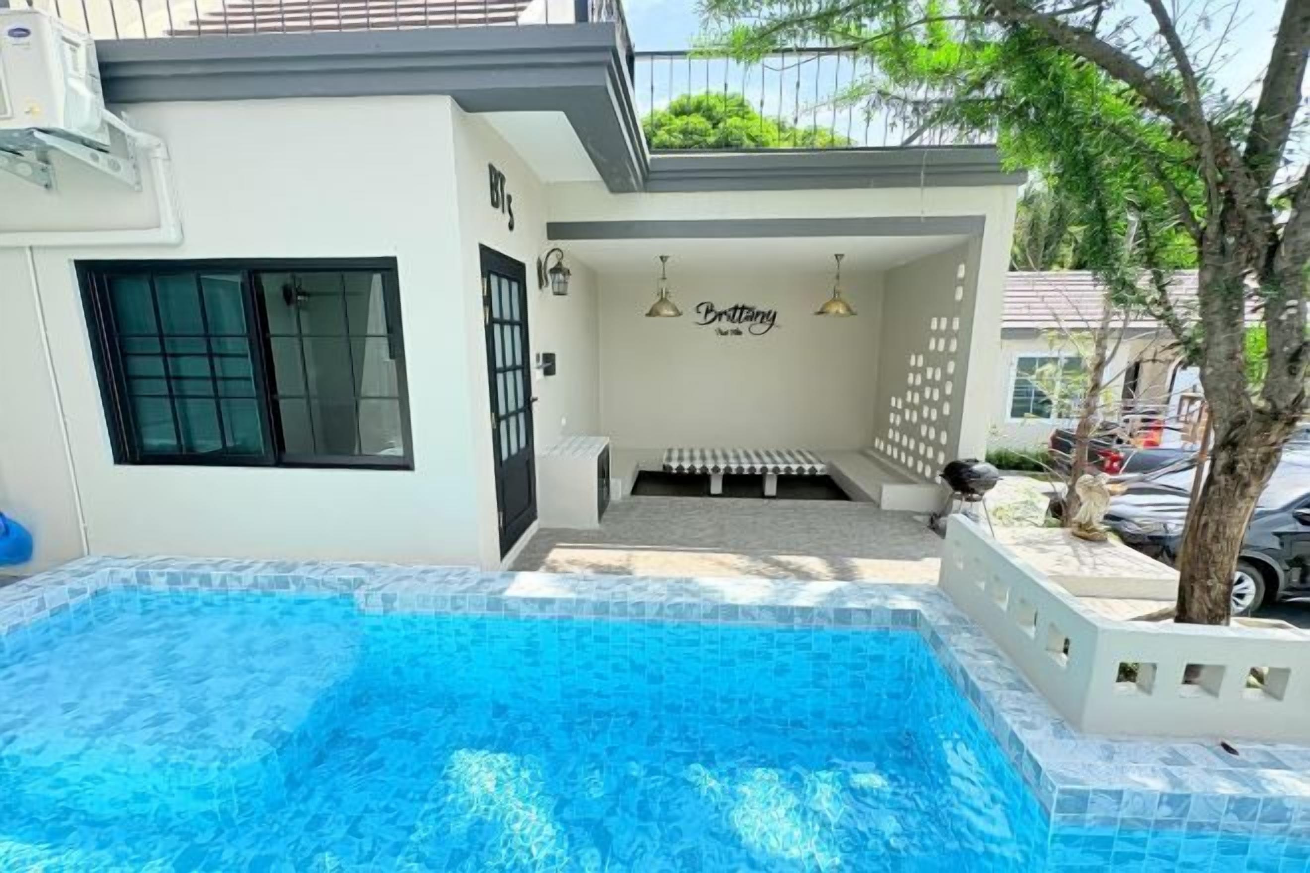 A swimming pool with a tiled deck, a covered seating area, and a wall with a sign.