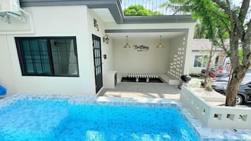 A swimming pool with a tiled deck, a covered seating area, and a wall with a sign.